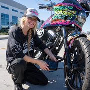 Person kneeling next to a motorcycle with colorful design, holding a phone.