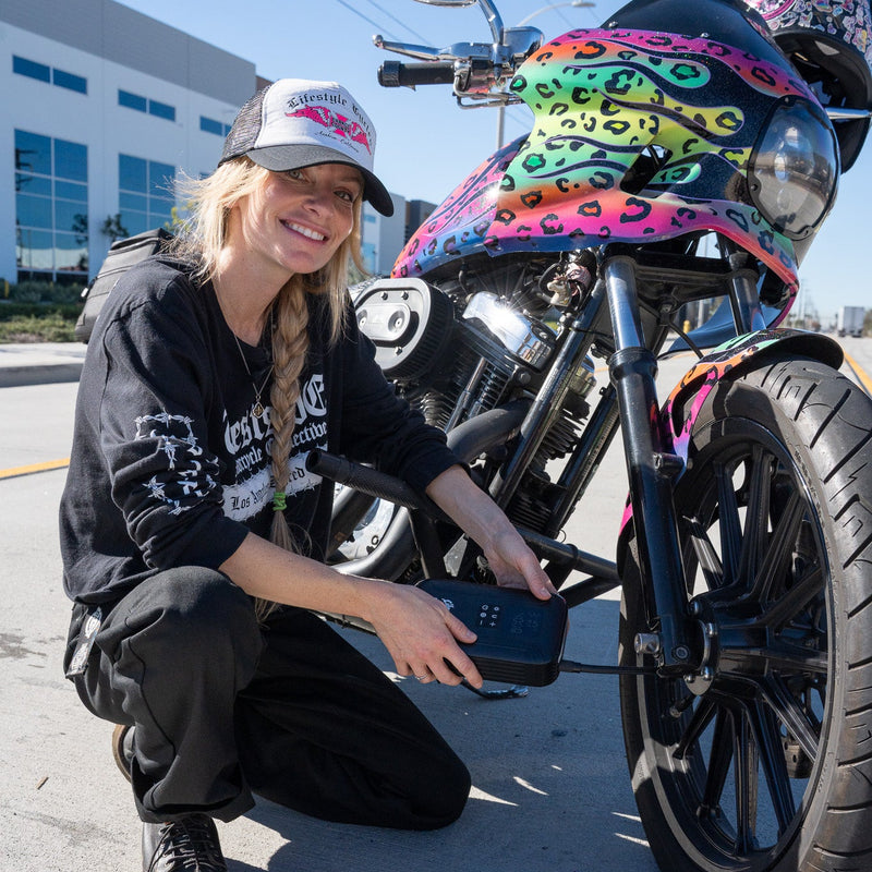 Person kneeling next to a motorcycle with colorful design, holding a phone.