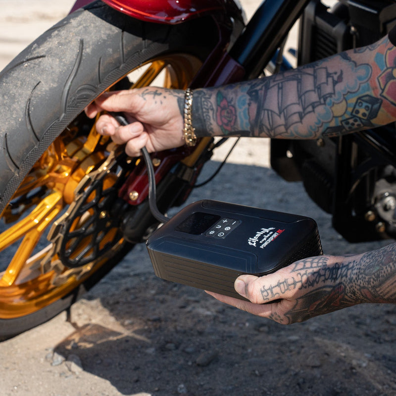 Person with tattoos using a jump starter on a motorcycle