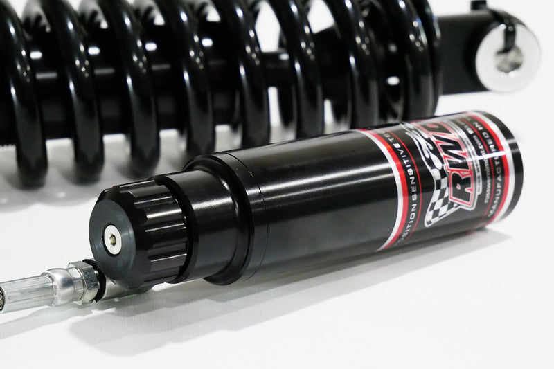 A close-up side shot of an RWD V-Twin RS-2 reservoir, featuring a black body with red and white RWD branding, connected to a silver hose, with a black spring in the background.